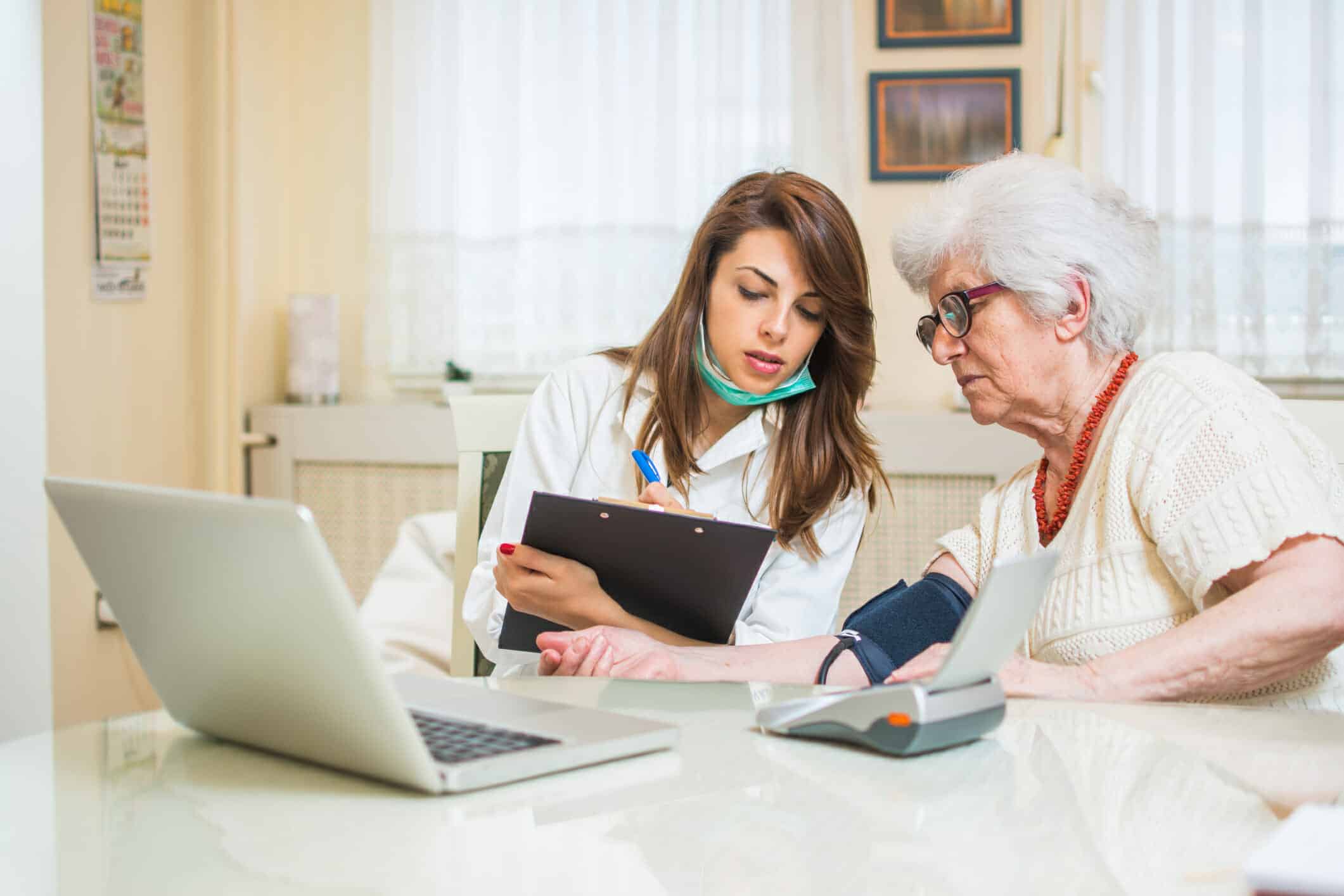 Eine Pflegekraft zeigt der Seniorin die Datenübertragung der Blutdruckwerte an den Arzt zur Fernbehandung