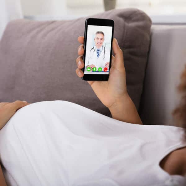 Schwangere auf Sofa und Videochat mit Arzt